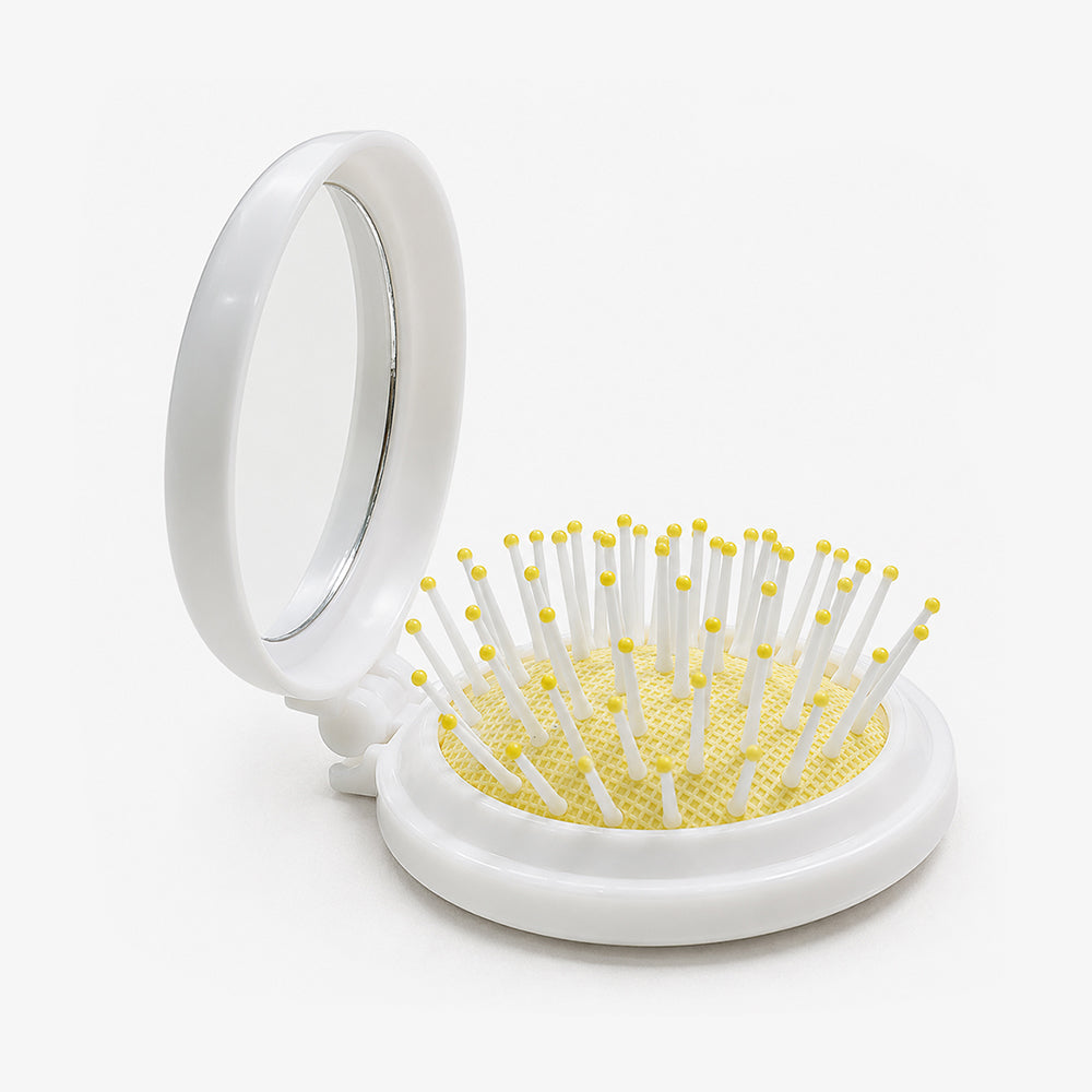 White folding hair brush with a built-in mirror, yellow cushioned base, and white bristles tipped in yellow