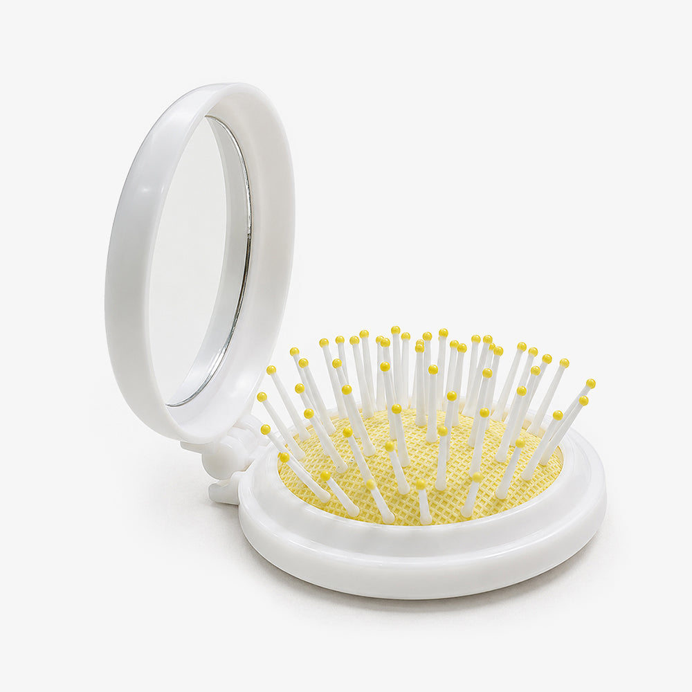 White folding hair brush with built-in mirror, yellow-tipped bristles, and mesh cushion base