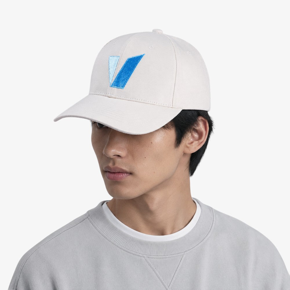 Classic six-panel baseball cap in off-white cotton twill with a curved brim and embroidered blue geometric detail on the front