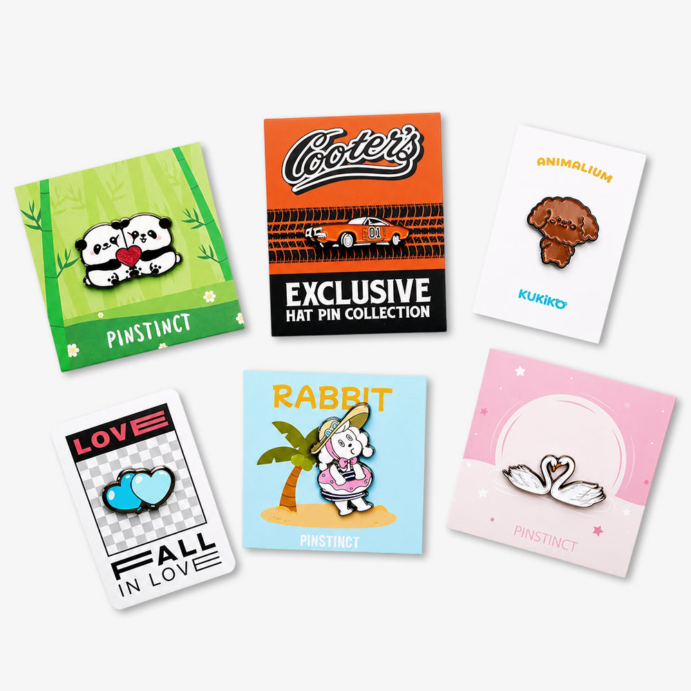 Backing cards for enamel pins in green, orange, white, black-checkered, blue, and pink with illustrated designs