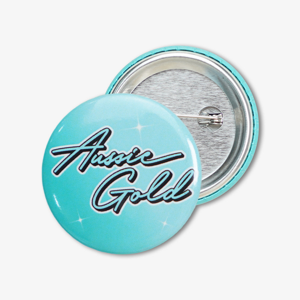 Round light blue button badge with "Aussie Gold" cursive print, showing front design and metal pin backing