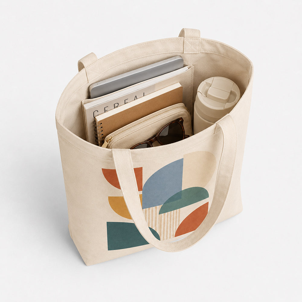 Beige canvas tote bag with bottom, printed with abstract geometric art, holding books, tumbler and sunglasses inside