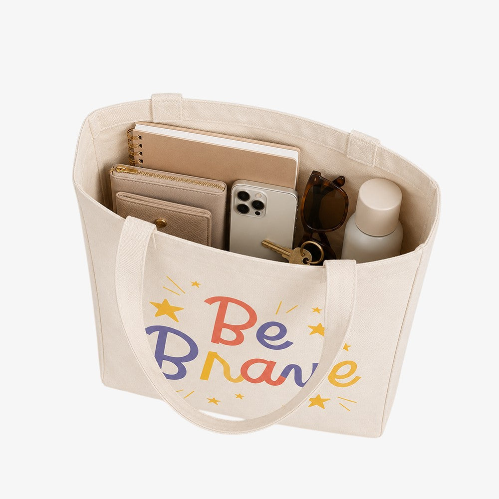 Canvas tote bag with side and bottom, beige printed with colorful "Be Brave" lettering, holding daily essentials inside
