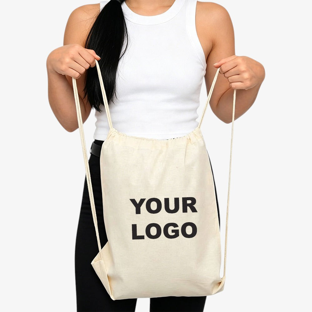 Cotton drawstring bag in natural beige, blank custom space for your printed logo, held by a woman