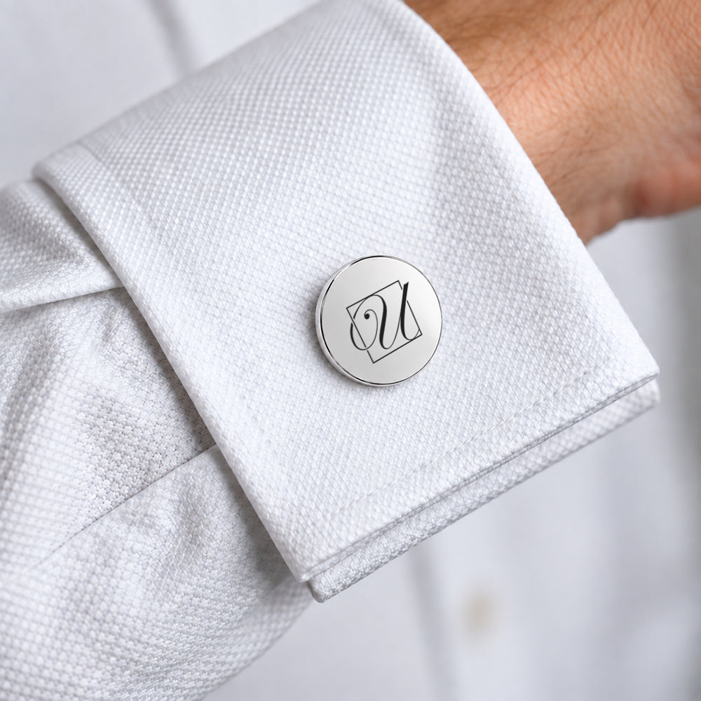 Silver round cufflinks with a polished finish and an engraved monogram design on a white shirt cuff