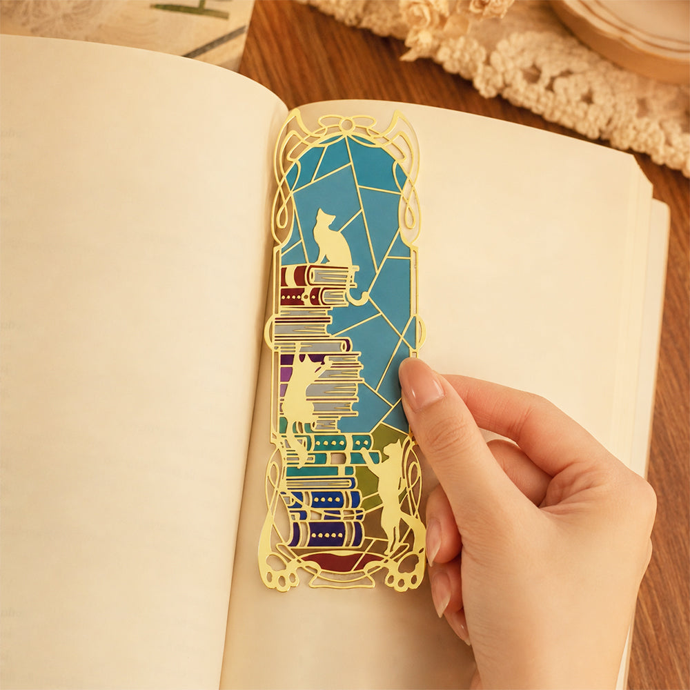 Custom hollow metal bookmark with colorful cat and book stack stained glass pattern, held on an open book page