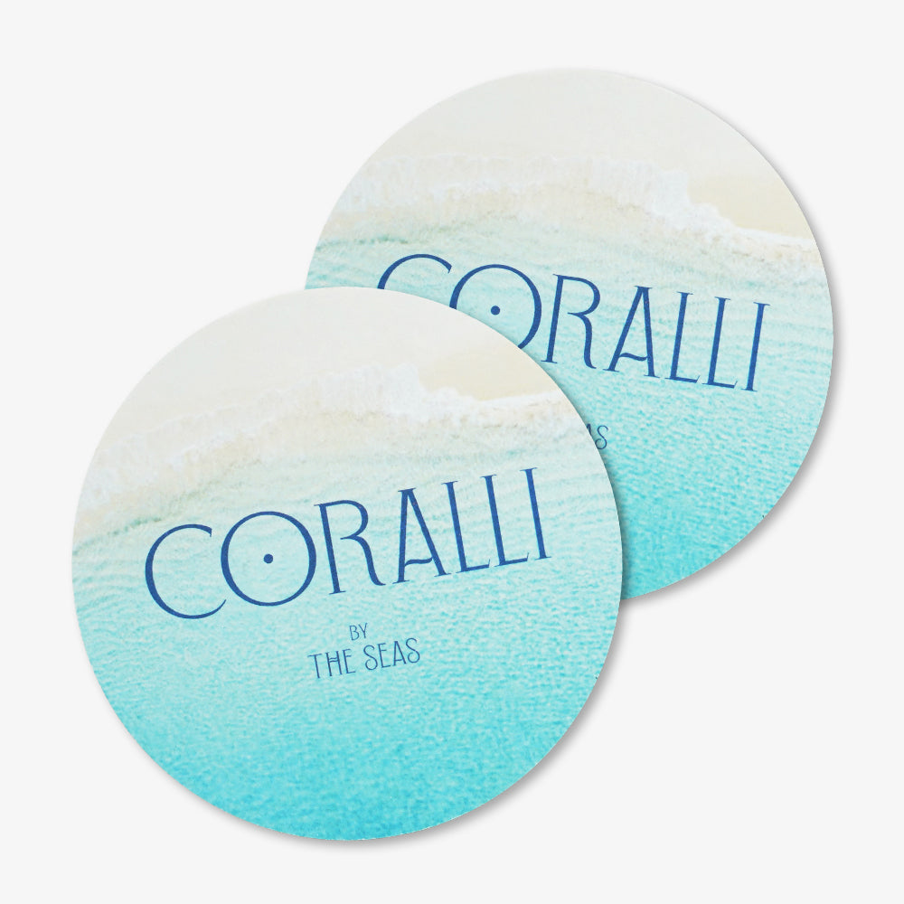 Two round custom pulpboard coasters printed with turquoise beach wave art and CORALLI brand text