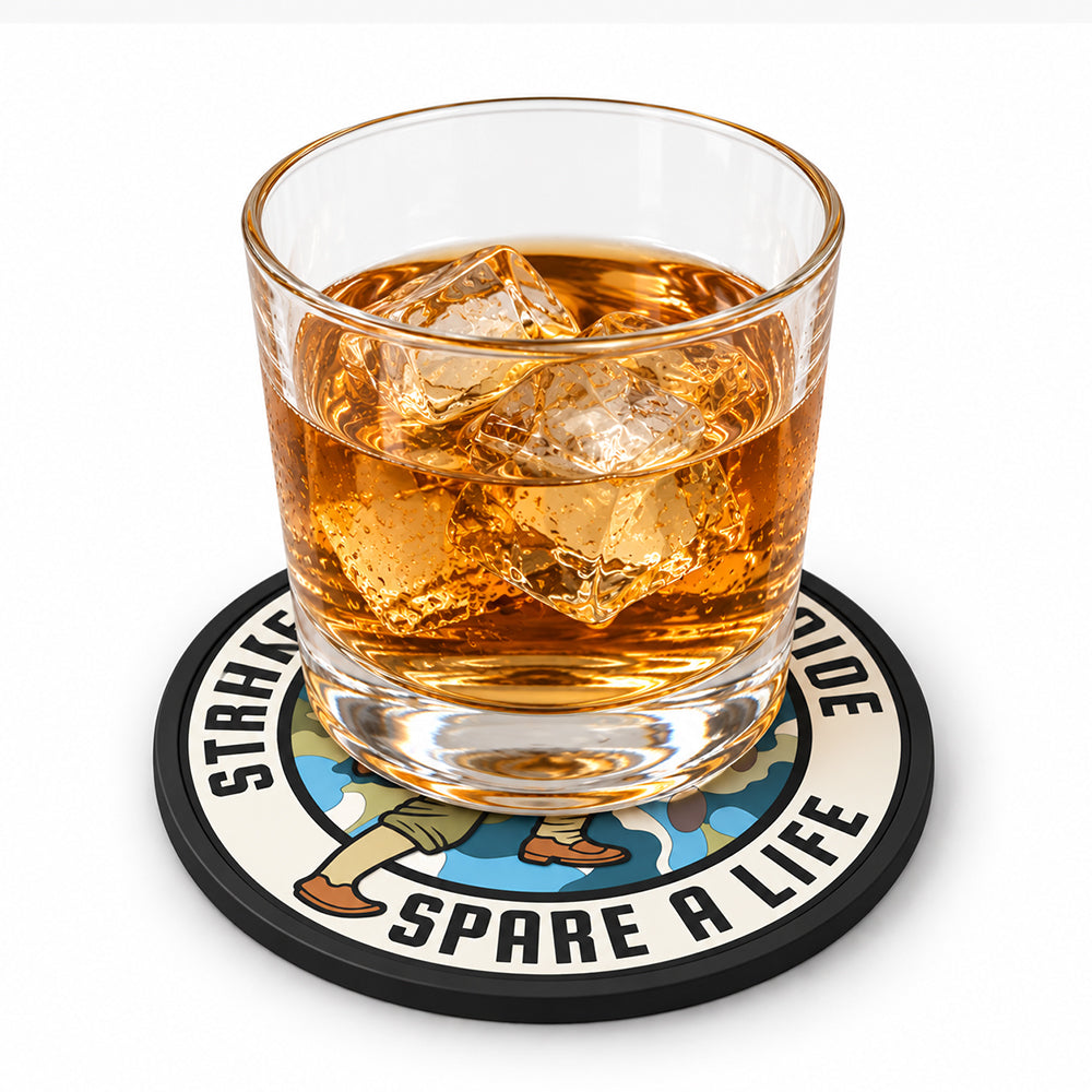 Round PVC coaster with black rim, cream center, and colorful illustrated design under a glass of amber liquid with ice