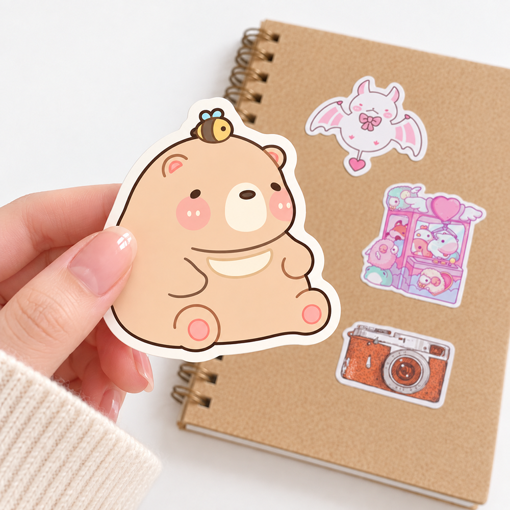 Die cut sticker of a smiling beige bear with pink cheeks and a tiny bee on its head