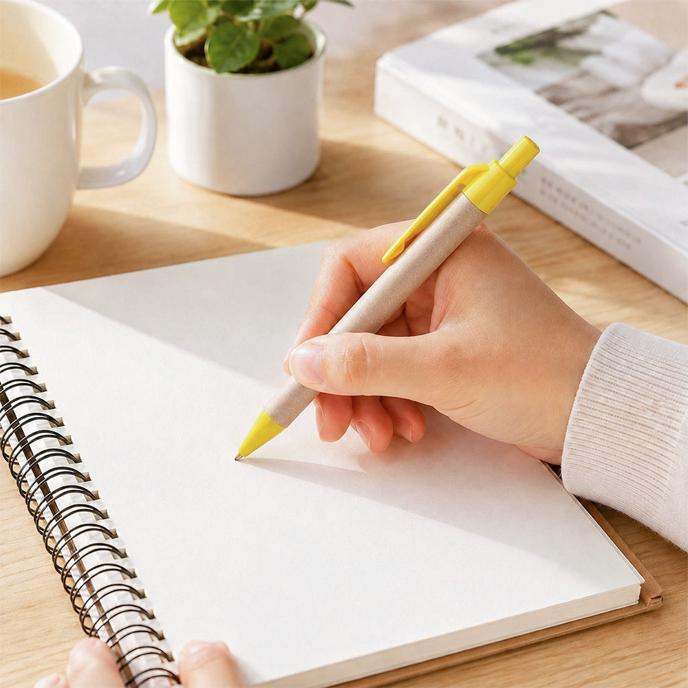 Yellow-accented paper barrel ballpoint pen with clip, held over a spiral notebook