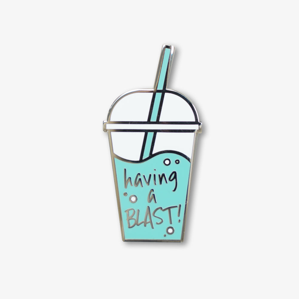 Hard enamel pin shaped like a takeaway iced drink cup, light blue with "having a blast!" text and polished silver metal outline