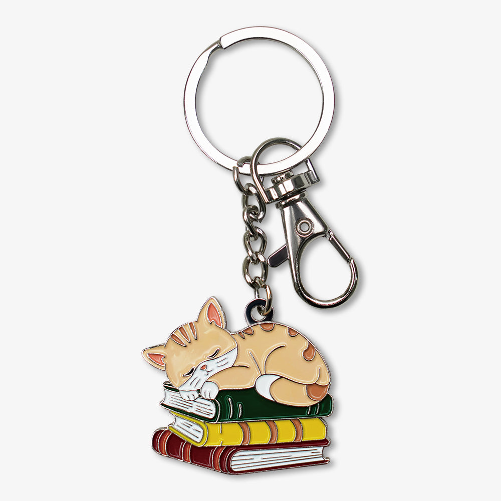Metal enamel keychain featuring a cute sleeping orange tabby cat on stacked books, with silver key ring and lobster clasp