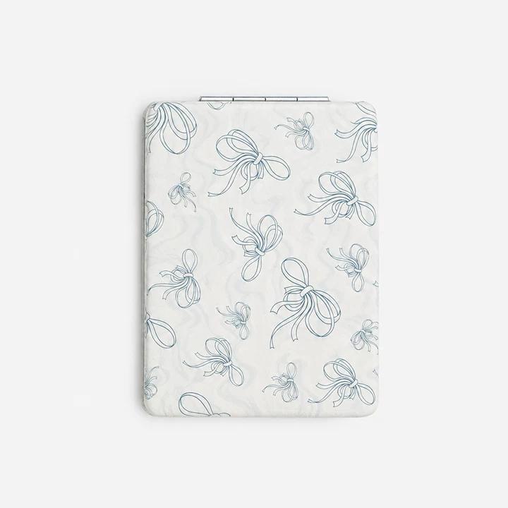 Folding compact mirror with white PU leather cover featuring a delicate blue ribbon pattern and a slim metallic hinge