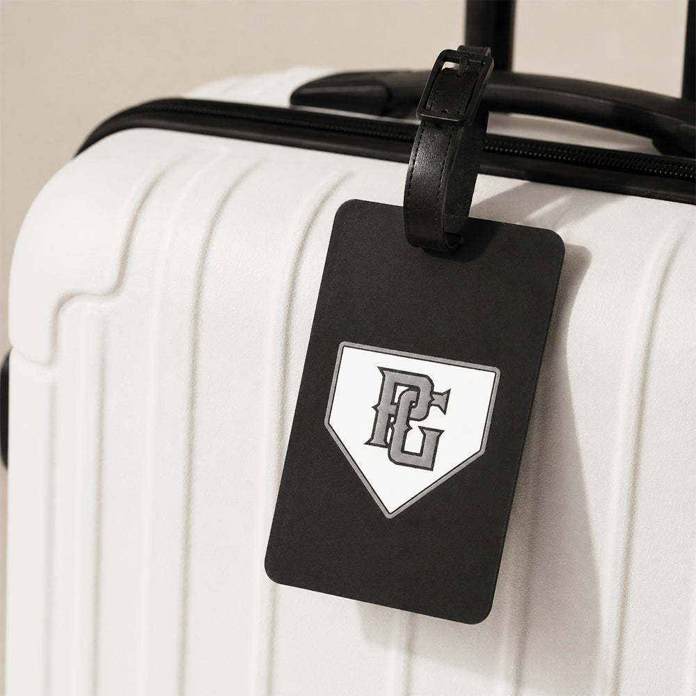 Black PVC luggage tag with custom PC logo, attached to a white hard-shell travel suitcase