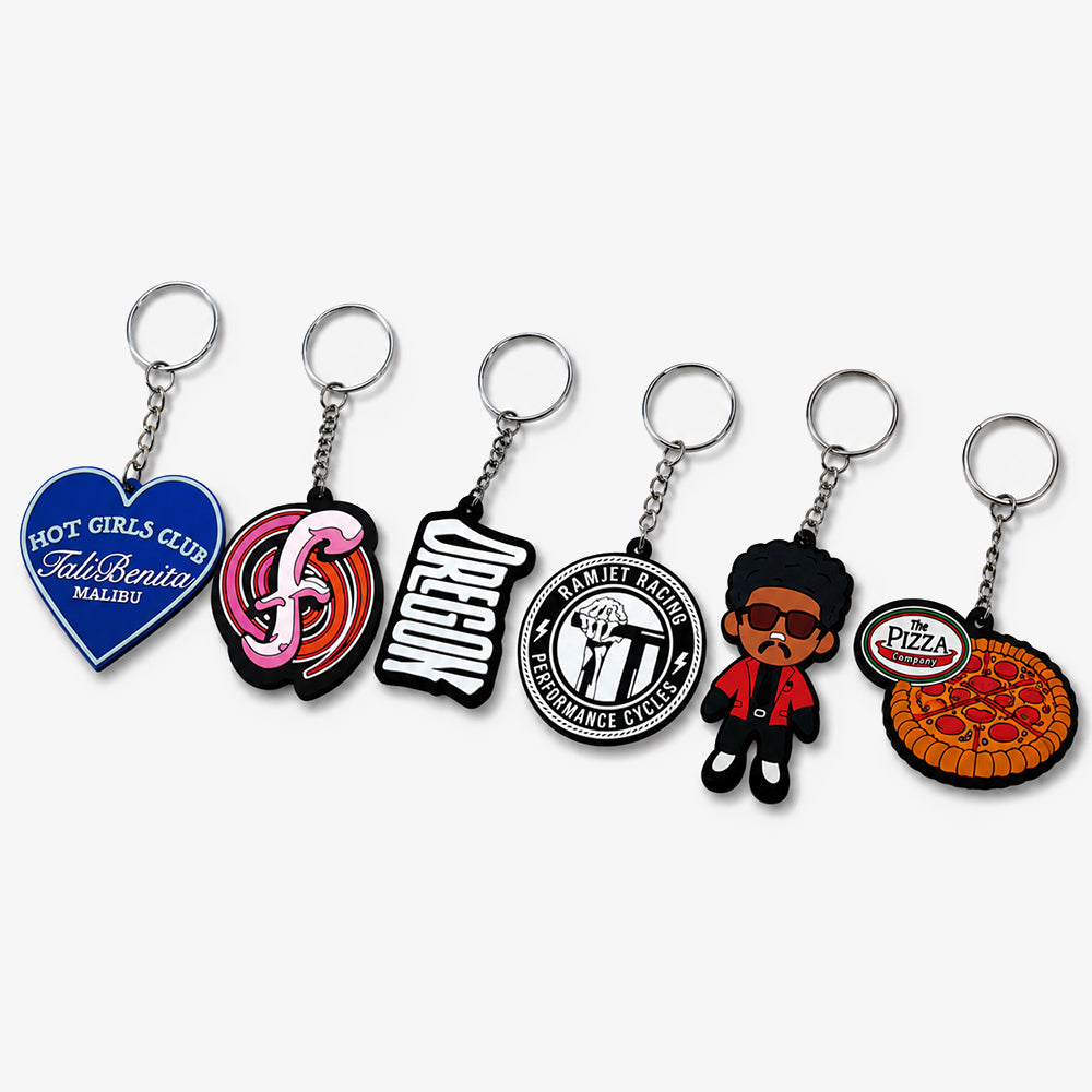 PVC rubber keychains in assorted custom shapes, including heart, cartoon character, pizza and logo prints, against white background