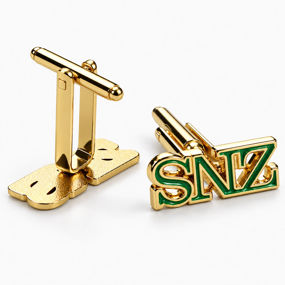 Gold-tone cufflinks with green soft enamel lettering and a polished bar toggle closure