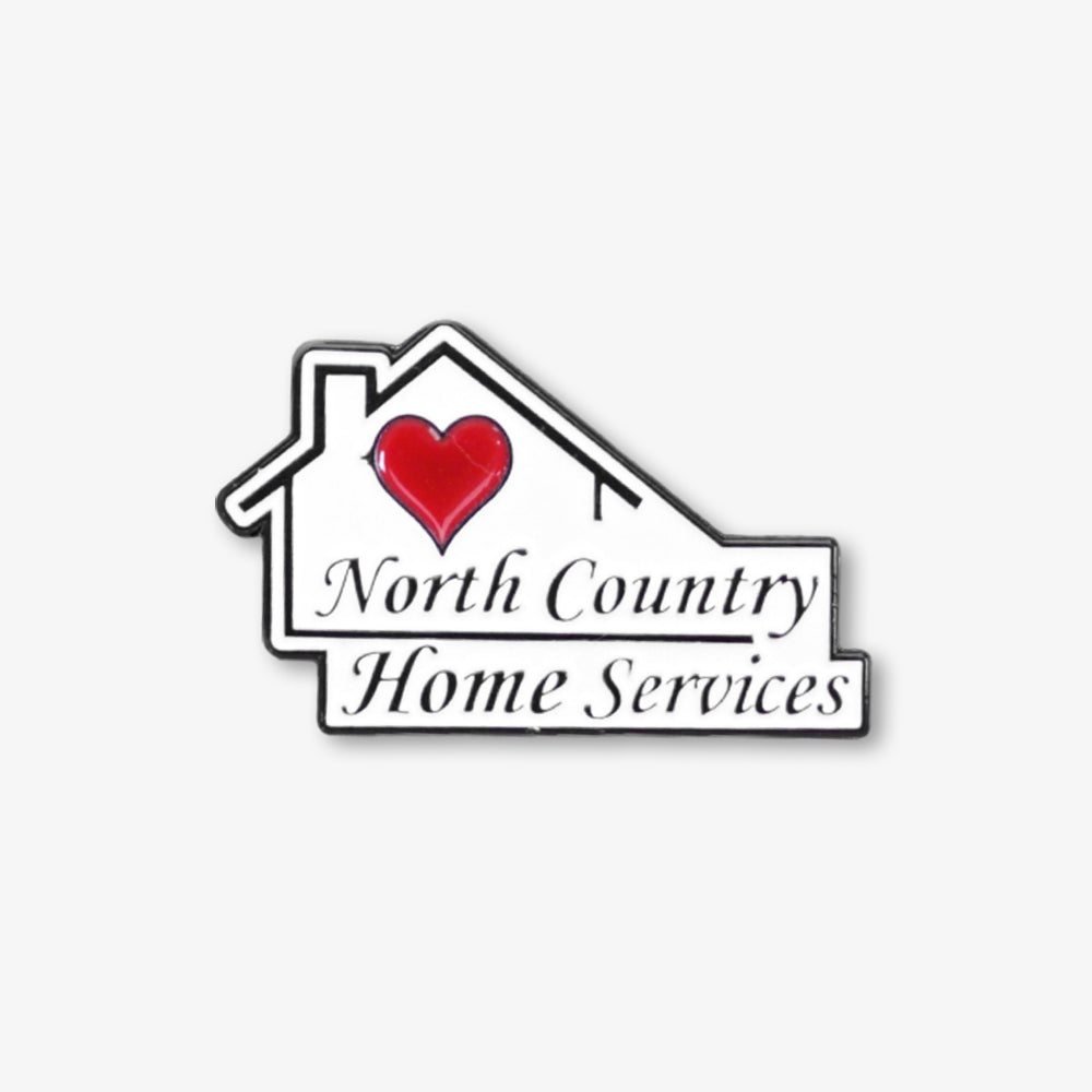 Soft enamel pin shaped like a house, with glossy red heart and North Country Home Services branding, white base with black trim