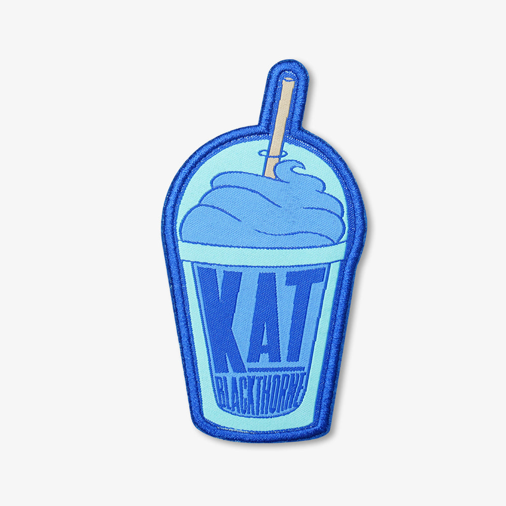Woven patch shaped like blue frothy milkshake cup, embroidered with KAT Blackthorne lettering and straw detail